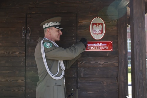 Gen. bryg. SG dr Piotr Boćko przykręca metalową tabliczkę z napisem "K.O.P. POSTERUNEK". 