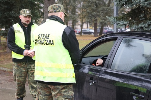 Dwóch funkcjonariuszy stoi przy pojeździe, w którym siedzi osoba Dwóch funkcjonariuszy stoi przy pojeździe, w którym siedzi osoba