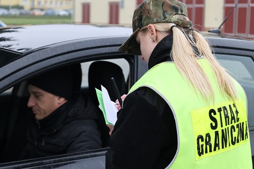 Funkcjonariuszka stojąca przy pojeździe, w którym siedzi mężczyzna Funkcjonariuszka stojąca przy pojeździe, w którym siedzi mężczyzna